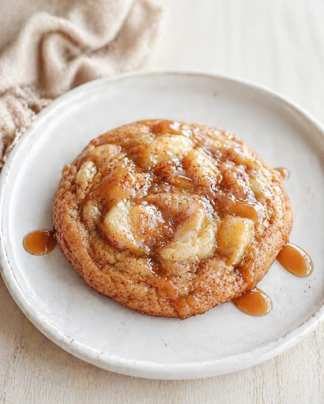 A banana-topped caramel cinnamon roll served on a white plate with drizzle.