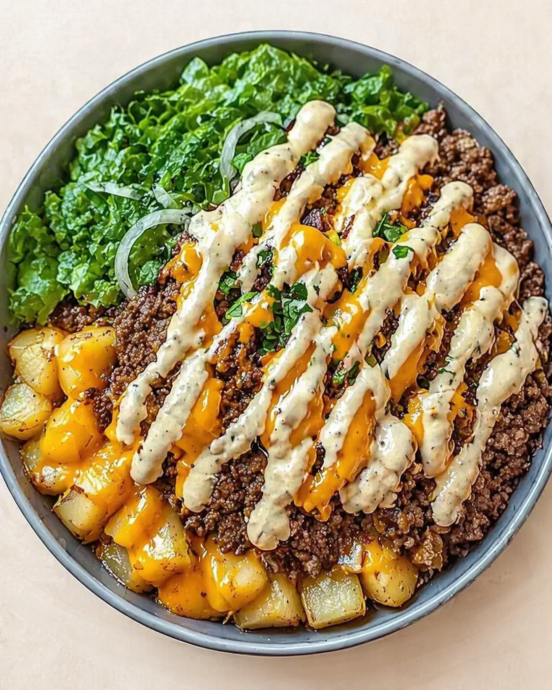 top-down view of a beef-potato-kale bowl with creamy drizzle and herbs