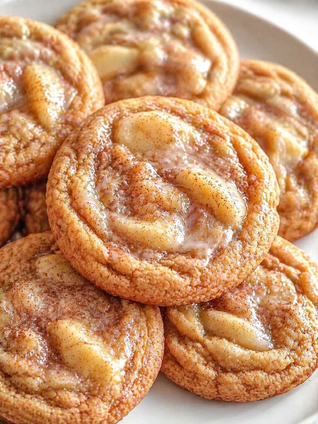 Close-up of golden-brown spiral cookies with glossy apple-filled centers on a white plate.