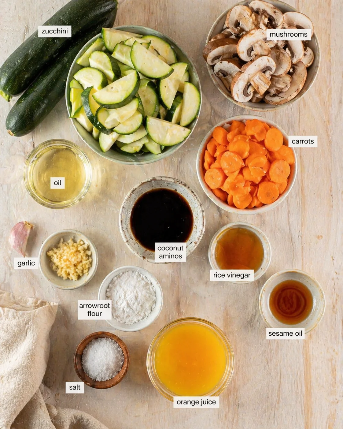 overhead view of ingredient mise-en-place: zucchini, mushrooms, carrots, oils, vinegars, garlic, and flour.