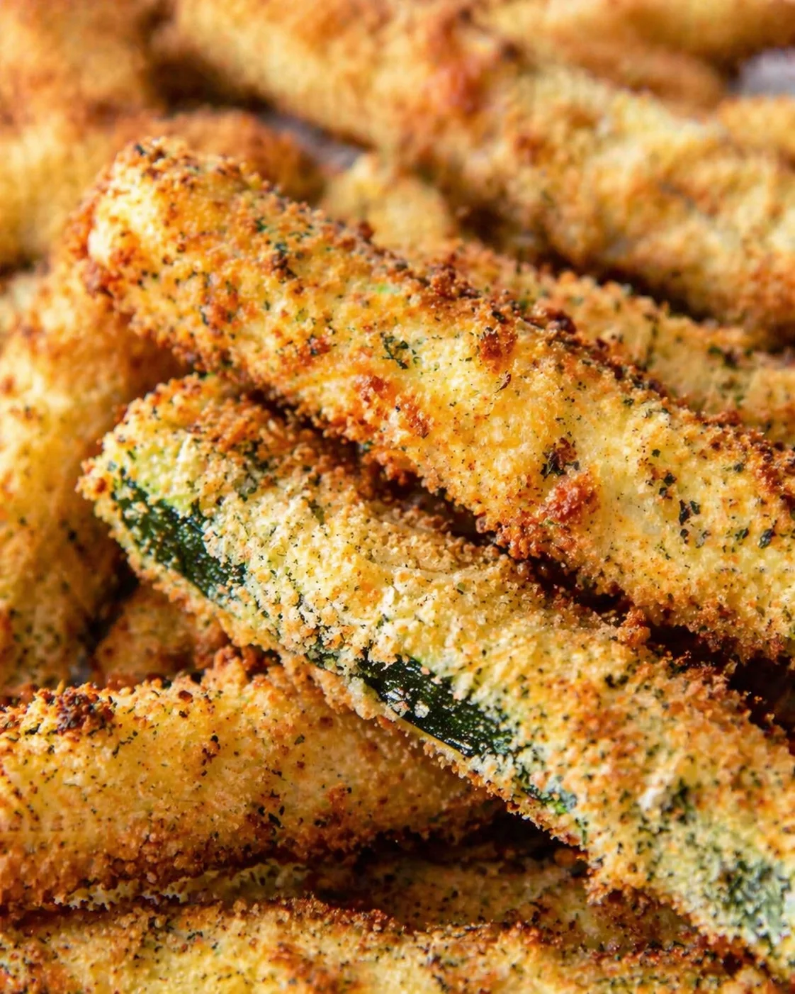 Close-up of crispy breadcrumb-coated zucchini sticks, golden brown with herb-speckled coating.