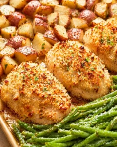 Golden-brown breaded chicken fillets with roasted potato cubes and green beans on a baking tray.