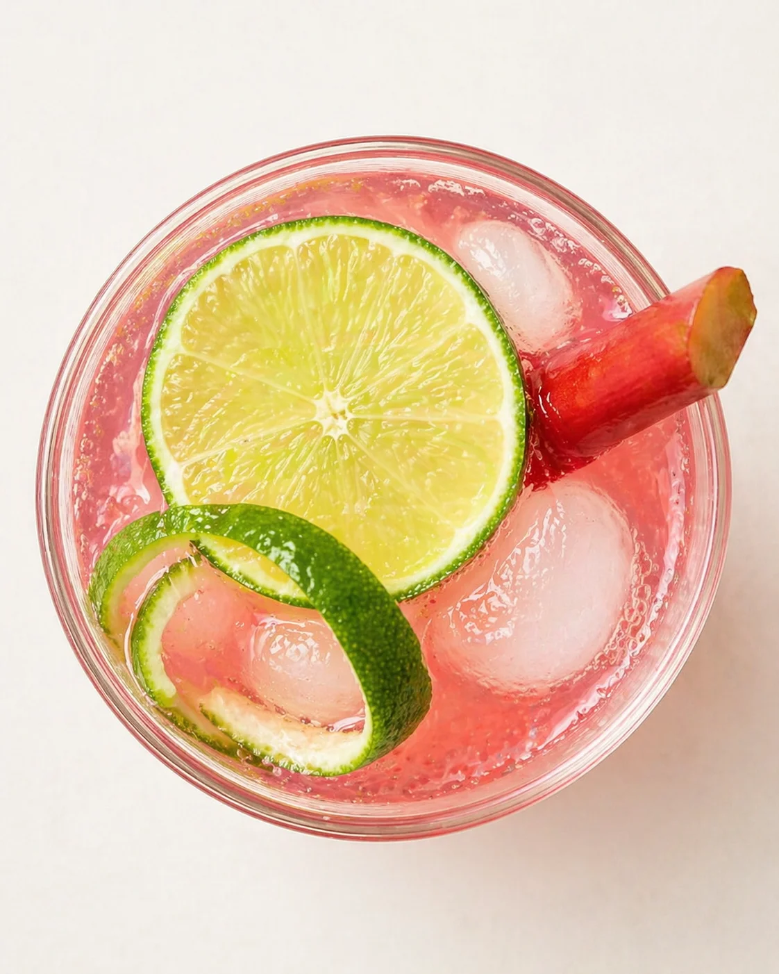 top-down view of pink cocktail with lime wheel garnish and curled lime peel in a glass