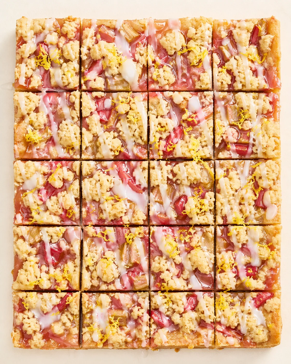 Top-down view of square rhubarb streusel bars with pink jam, crumb topping, and lemon zest.