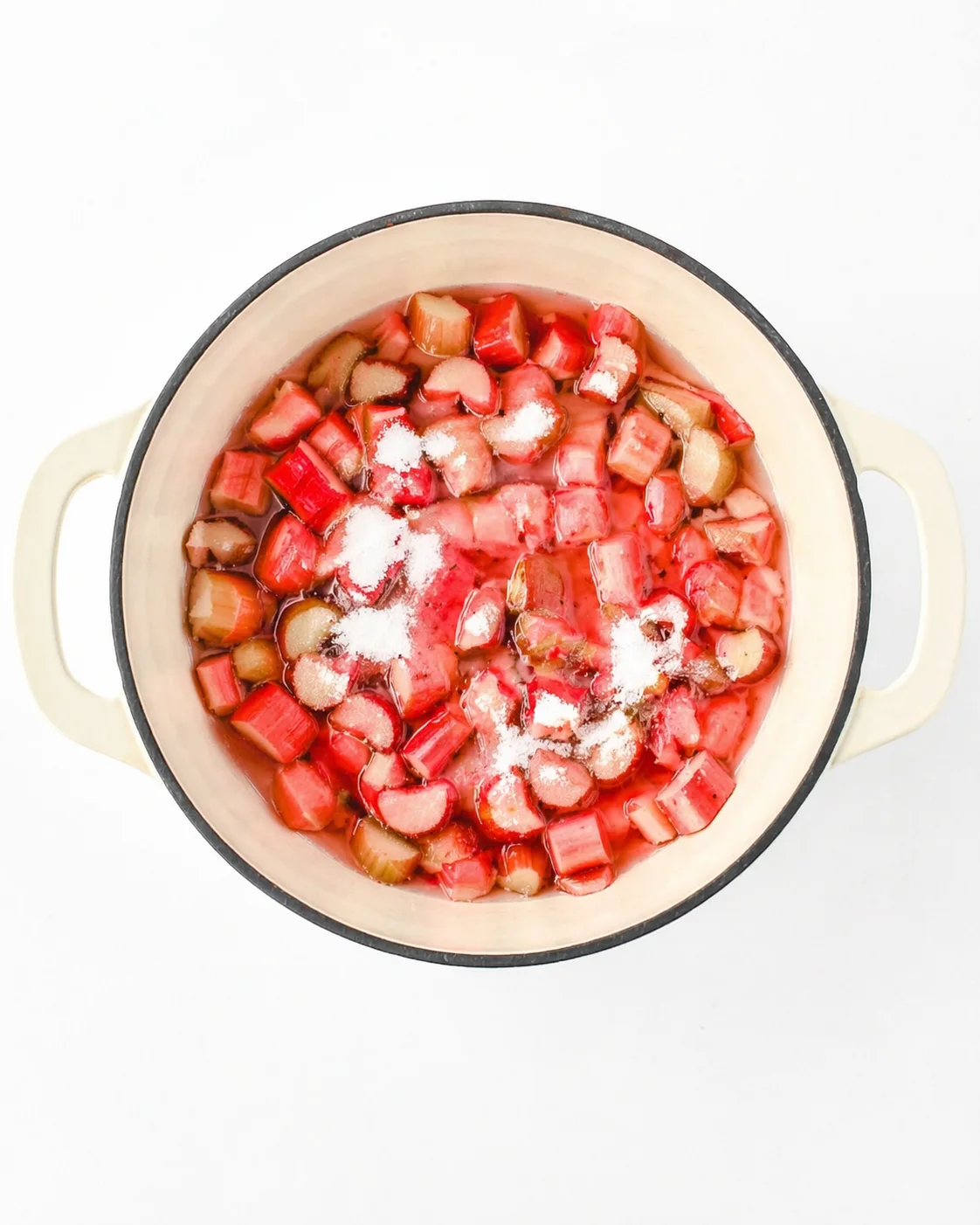Overhead view of a cream enamel pot filled with chopped rhubarb and sugar, ready to simmer.