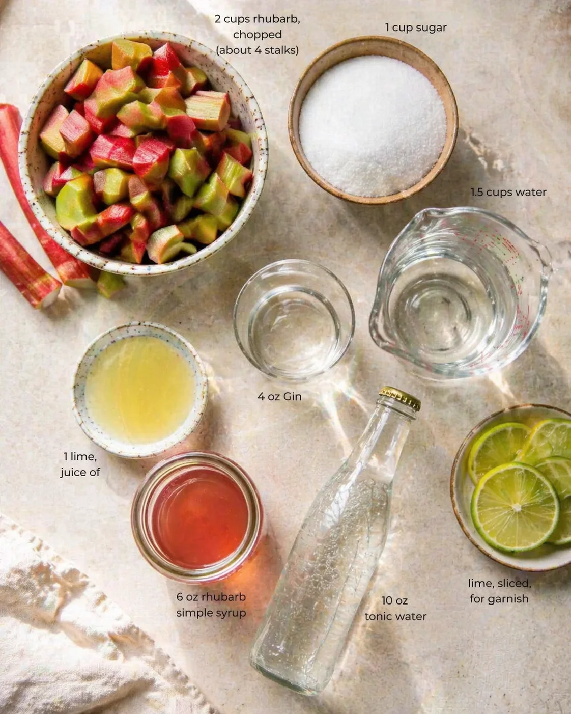 Overhead view of rhubarb cocktail ingredients, including chopped rhubarb, sugar, gin, tonic, lime juice, and lime slices.