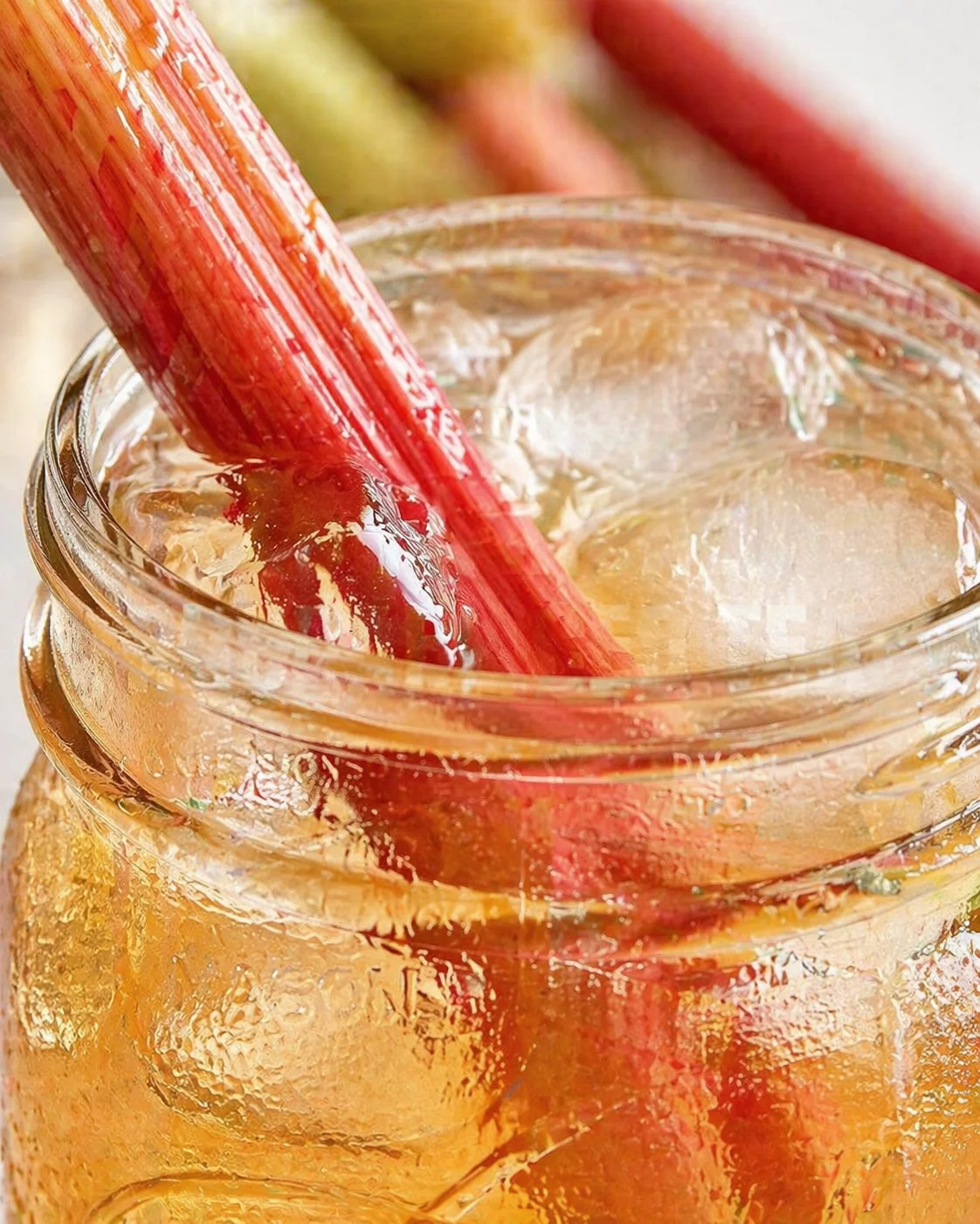 Close-up of a mason jar filled with iced tea and ice, with a red rhubarb stalk resting inside.