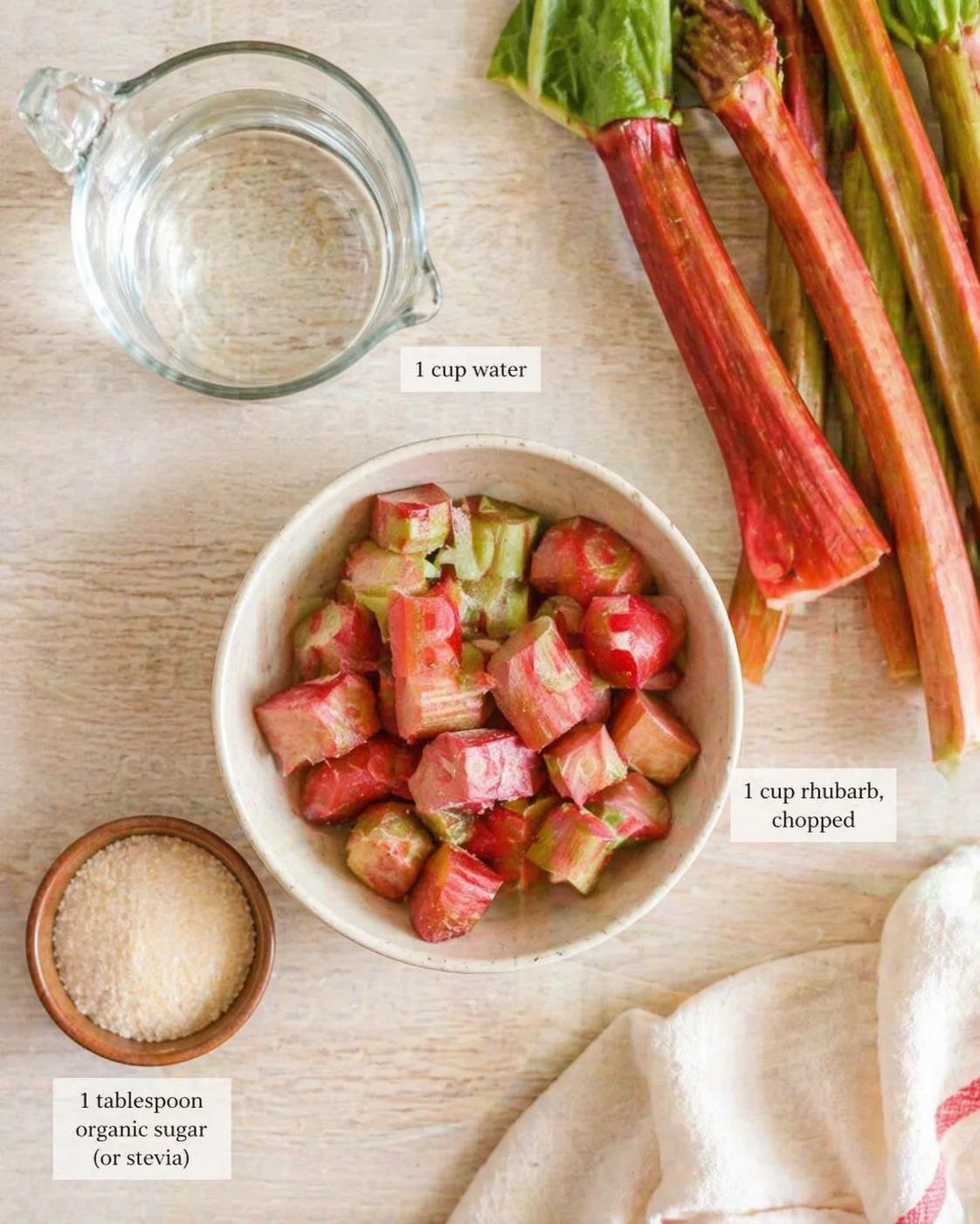 Overhead view of rhubarb stalks, chopped rhubarb in a bowl, water measuring cup, and sugar on a light wooden surface.