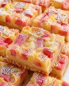 Close-up of rhubarb-lemon bars with powdered sugar and crumb crust.