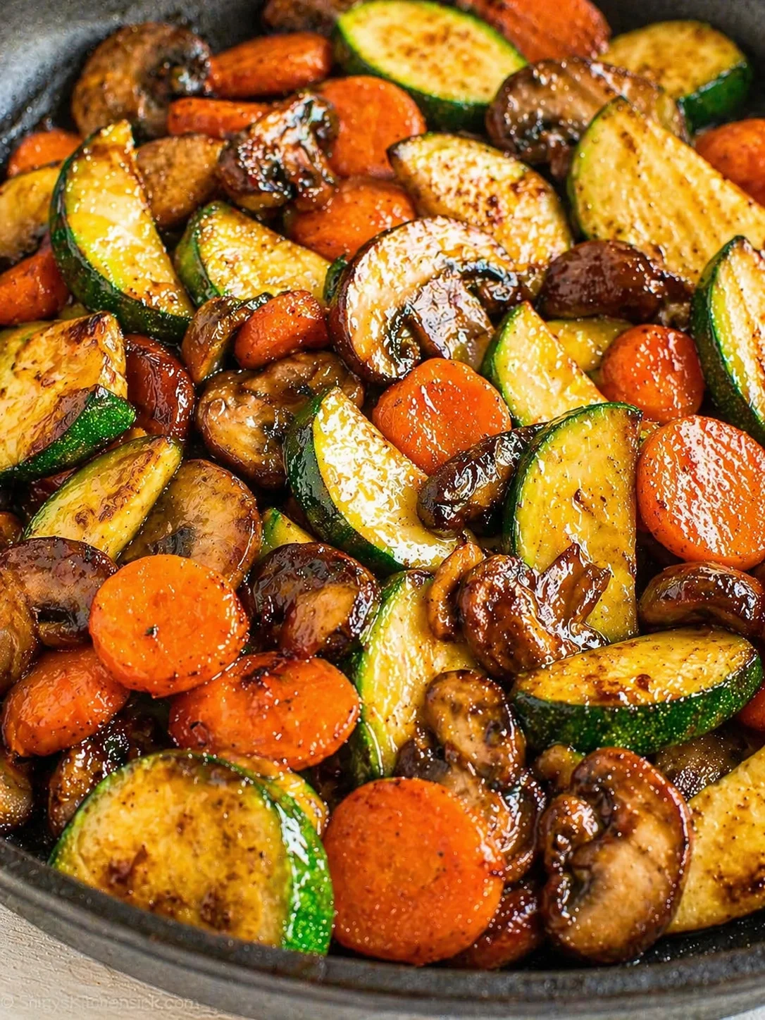 Close-up of glossy roasted zucchini, carrot, and mushroom medley in a skillet.