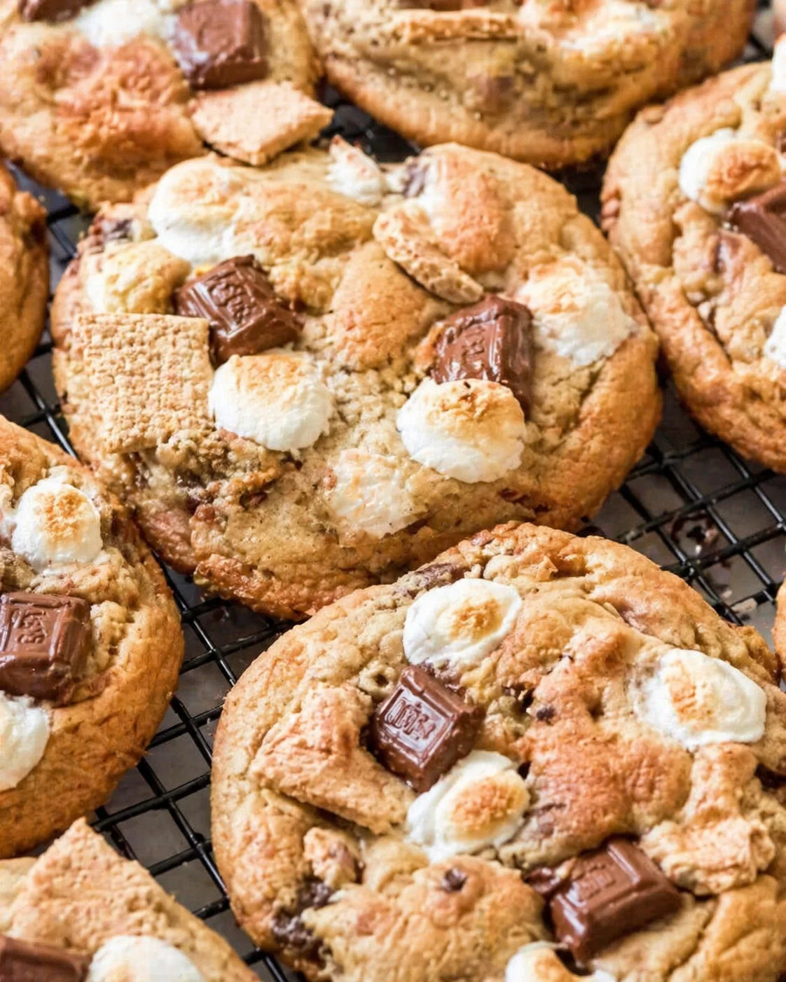 Golden cookies topped with toasted marshmallows and chocolate chunks on a cooling rack