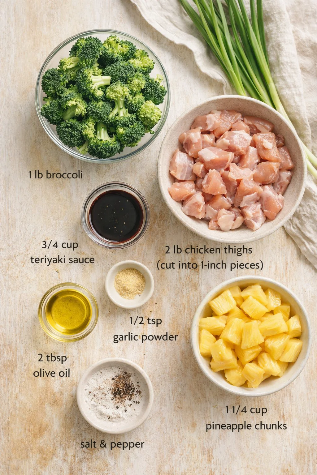 Overhead shot of broccoli, diced chicken, pineapple chunks, and sauces arranged on a light wooden surface with a linen cloth.