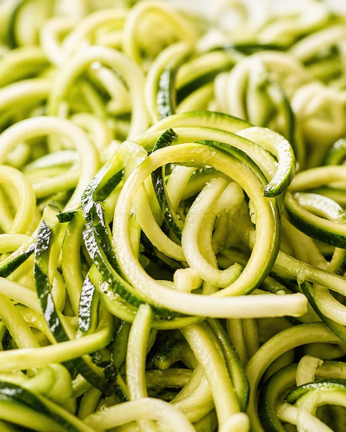 Close-up of tangled zucchini noodles, light-green ribbons glistening with moisture.