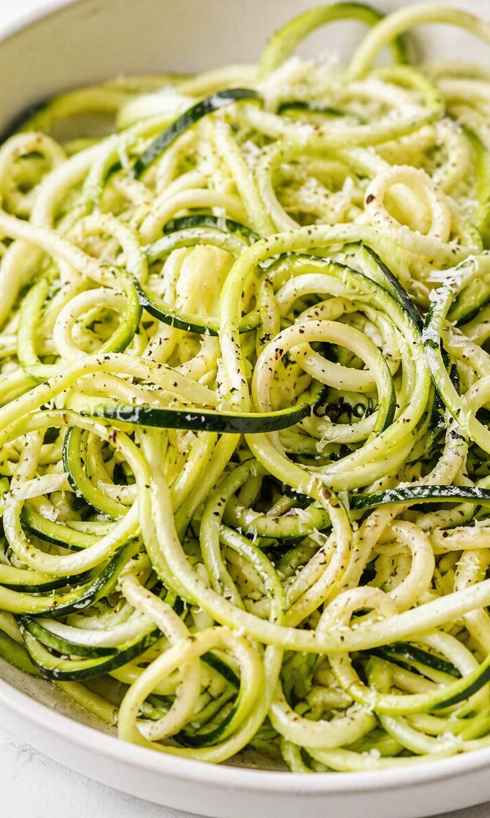 bowl of zucchini noodles sprinkled with grated cheese and fresh herbs