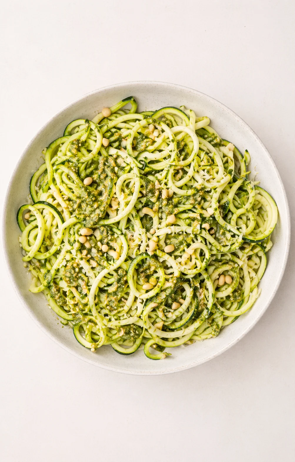 zucchini noodles with green pesto and pine nuts in a light bowl.
