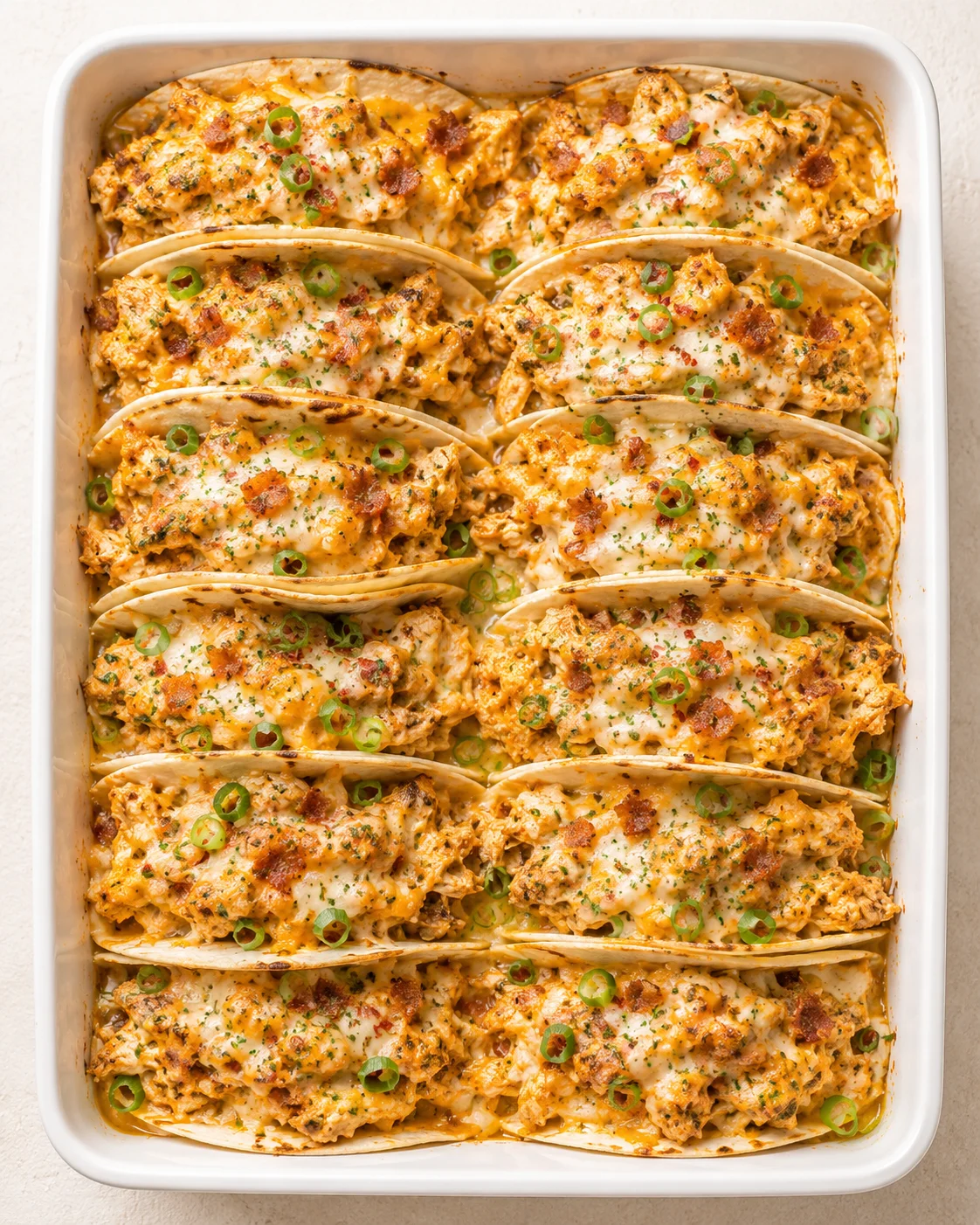 top-down view of a white baking dish filled with cheesy enchiladas topped with green onions