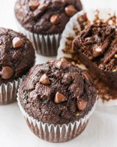 Close-up of chocolate muffins with chips in paper liners on a light wooden surface.
