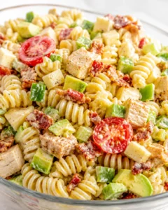 Creamy fusilli pasta tossed with chicken, avocado, bacon bits, and cherry tomatoes in a glass bowl.