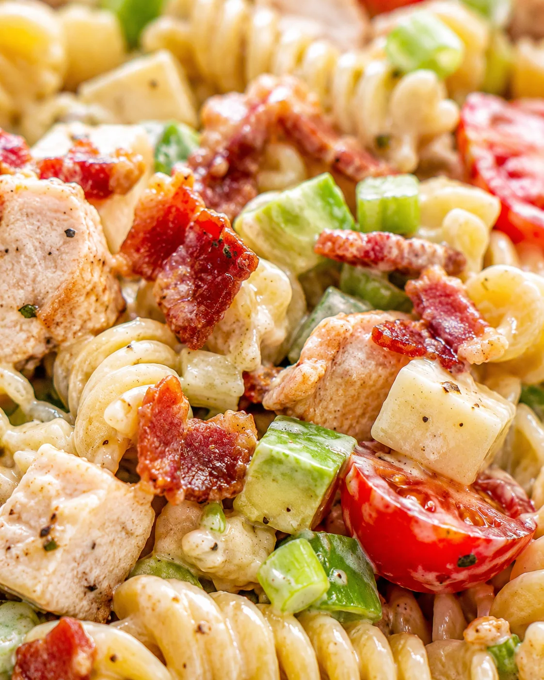 Close-up of creamy pasta salad with fusilli, crispy bacon, diced chicken, avocado, and tomato.