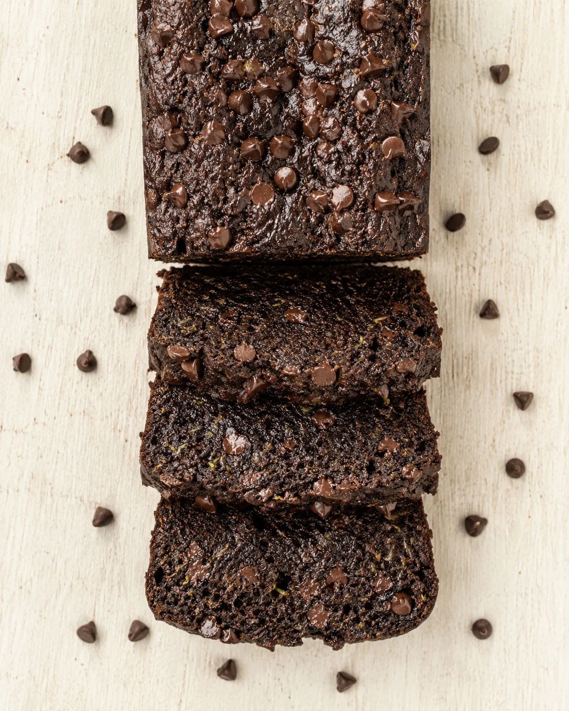 dense dark chocolate loaf sliced into pieces with chocolate chips on a light wood surface
