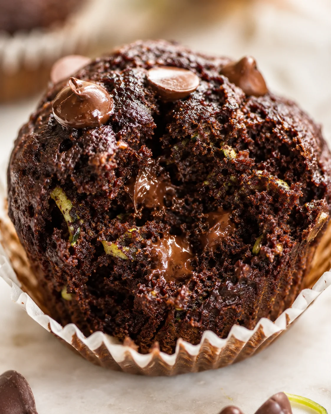 Close-up of a chocolate muffin with gooey center and melted chips in a white cupcake liner.
