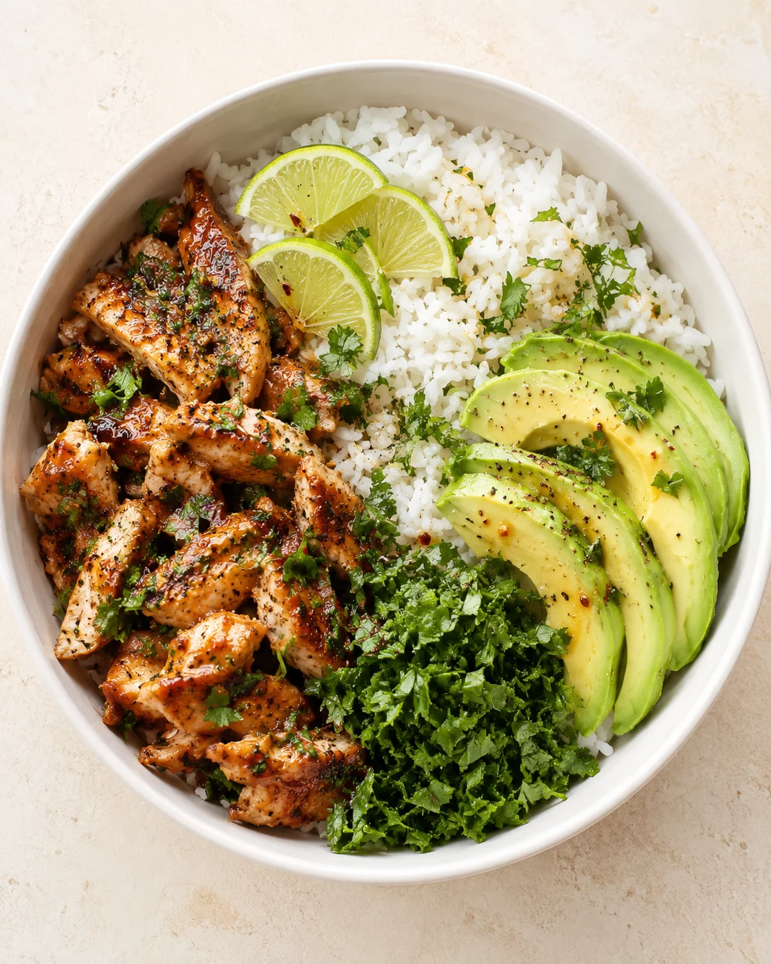 Top-down view of a bowl with rice, grilled chicken, avocado, lime wedges, and fresh herbs