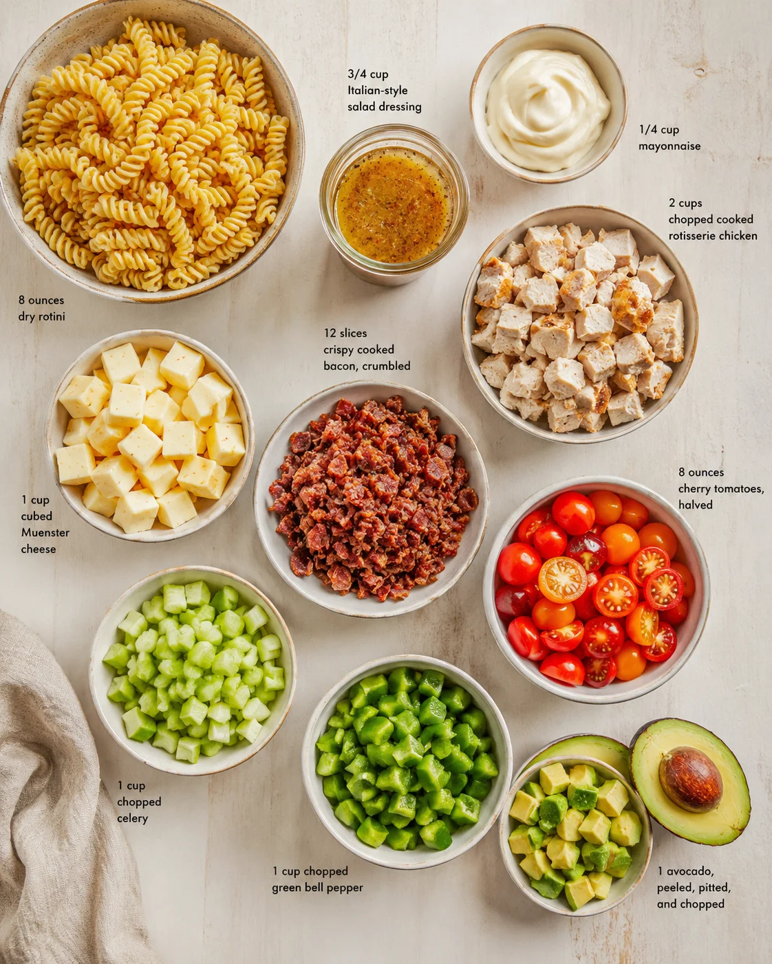 Overhead view of bowls with pasta, cheese, veggies, bacon, chicken, and dressings for a pasta salad.
