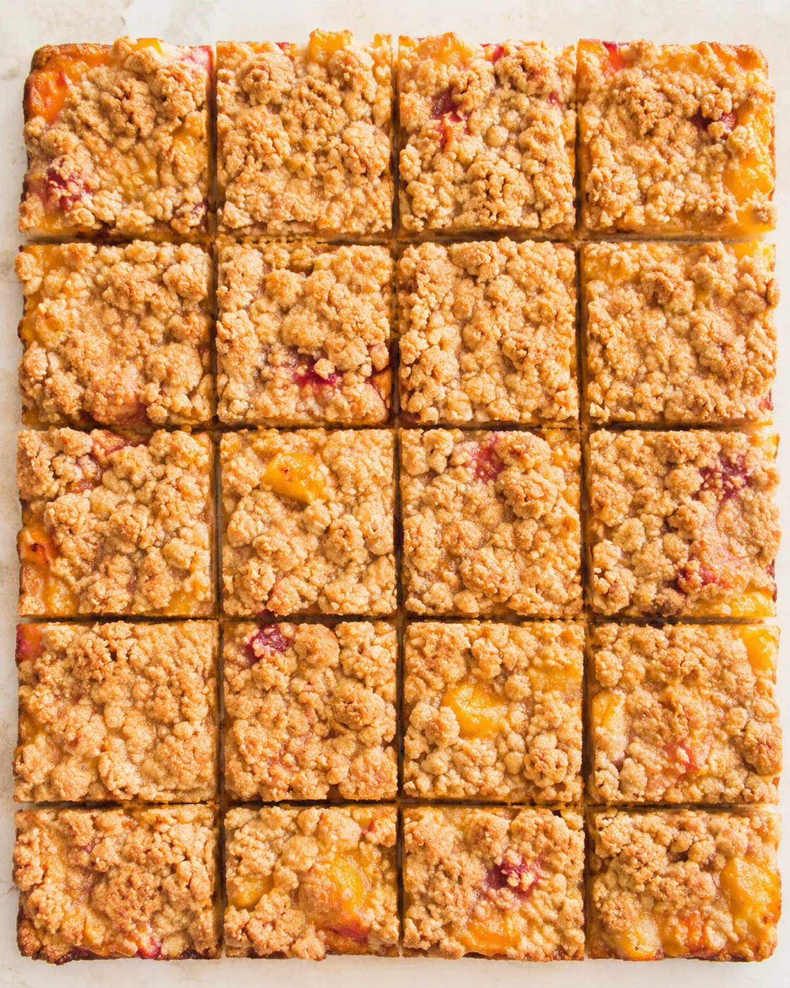 top-down view of a tray of peach crumble bars arranged in a 5x6 grid on parchment