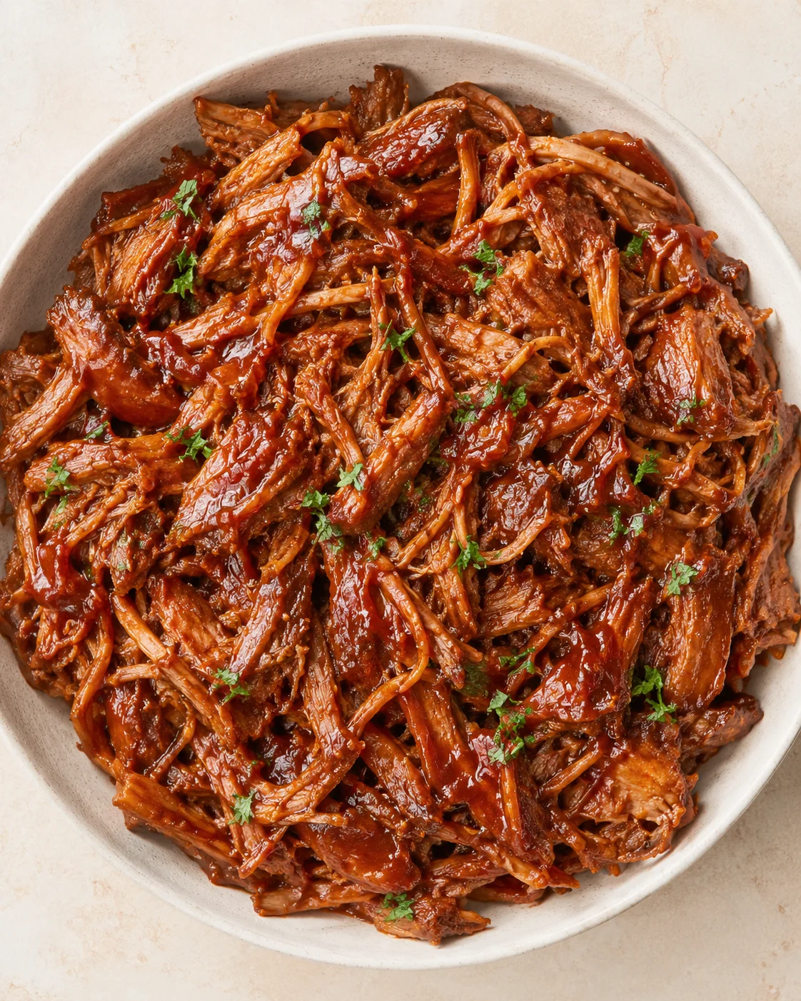 bowl of glossy shredded braised beef in barbecue sauce, garnished with parsley