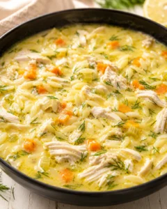 Creamy chicken and orzo soup with carrots and dill in a black pot.
