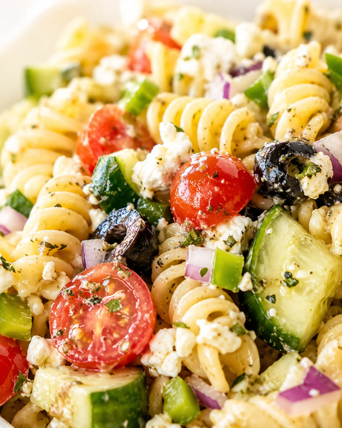 Close-up of colorful Mediterranean fusilli pasta salad with tomatoes, cucumber, olives, onion and feta.