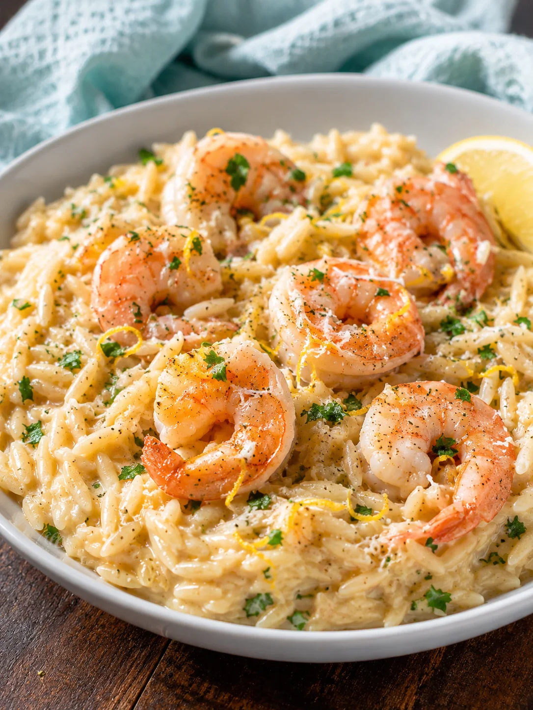 Creamy shrimp orzo served in a white bowl garnished with herbs and lemon wedge.