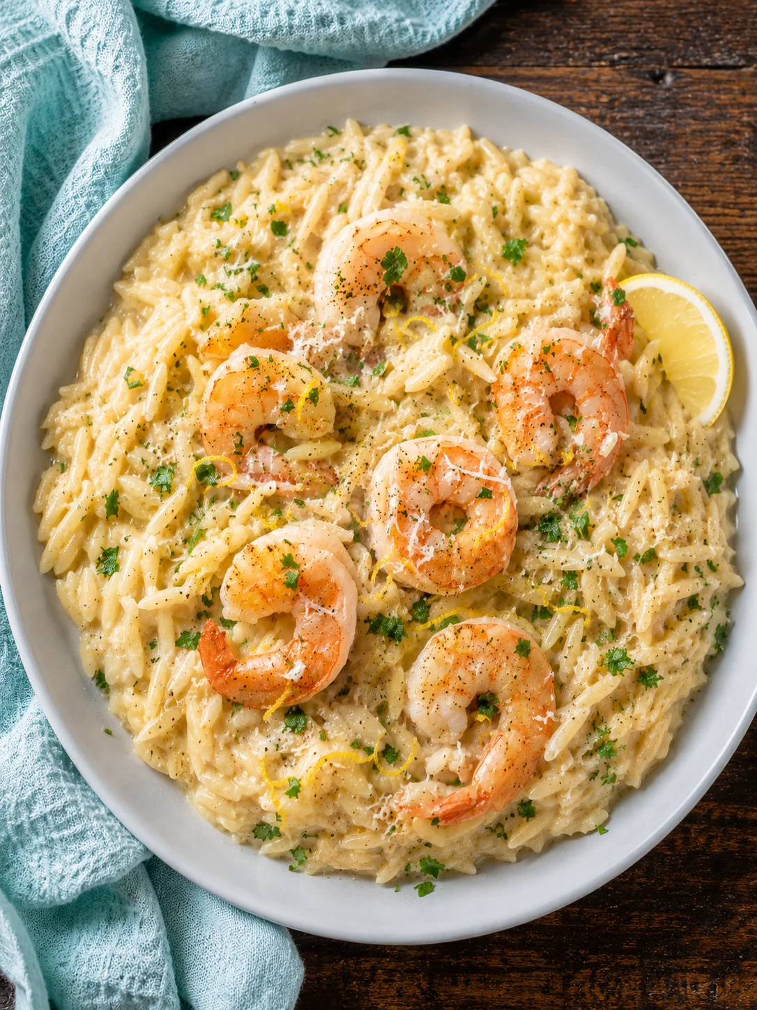 Creamy shrimp orzo served in a white bowl with lemon slices and herbs.