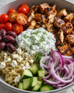 Colorful Mediterranean chicken bowl with vegetables, feta, and tzatziki sauce.