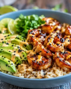 Close-up of teriyaki shrimp served with rice, avocado, and lime in a bowl.