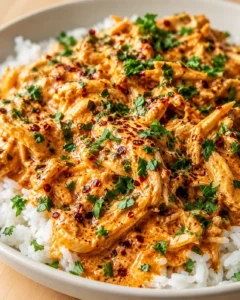 bowl of shredded chicken in creamy orange sauce, garnished with parsley over white rice