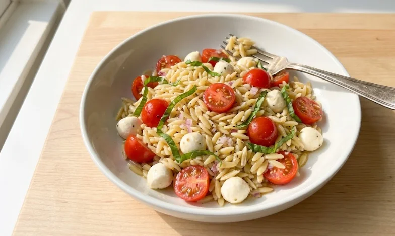 Colorful caprese orzo pasta salad with tomatoes, mozzarella, and basil in a white bowl.