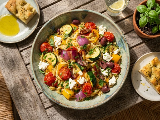Colorful roasted vegetable orzo salad served in a rustic bowl with fresh herbs.