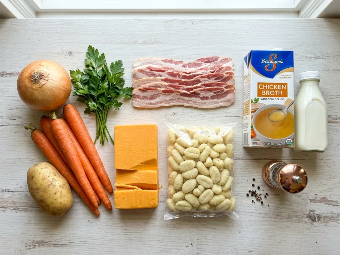 Ingredients for creamy bacon cheddar gnocchi soup arranged on a white surface.
