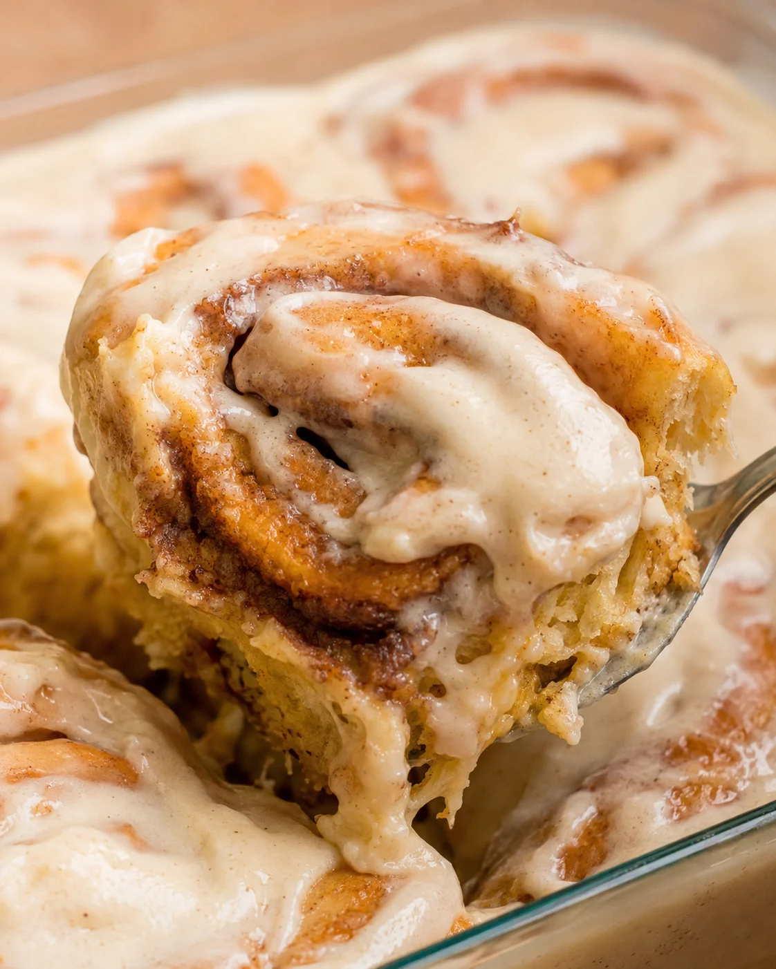 Close-up of a cinnamon roll with creamy frosting melting on top, fresh from baking.