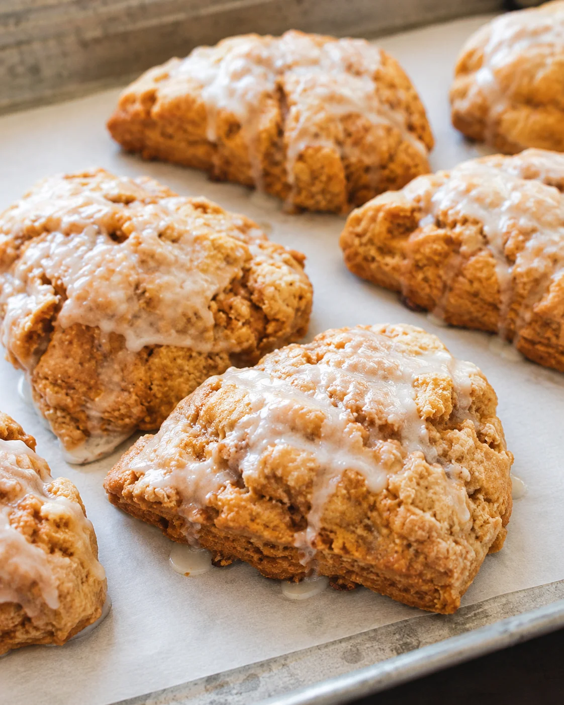 Freshly baked pumpkin scones topped with a sweet glaze on a baking sheet
