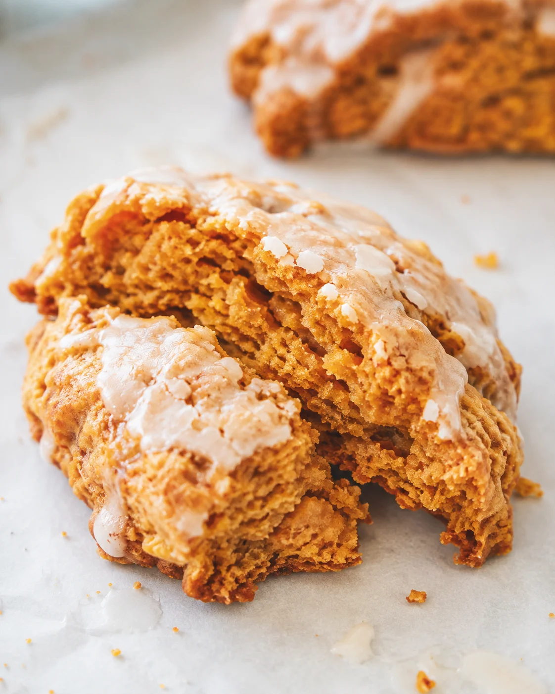 Golden pumpkin scones topped with sweet glaze on parchment paper