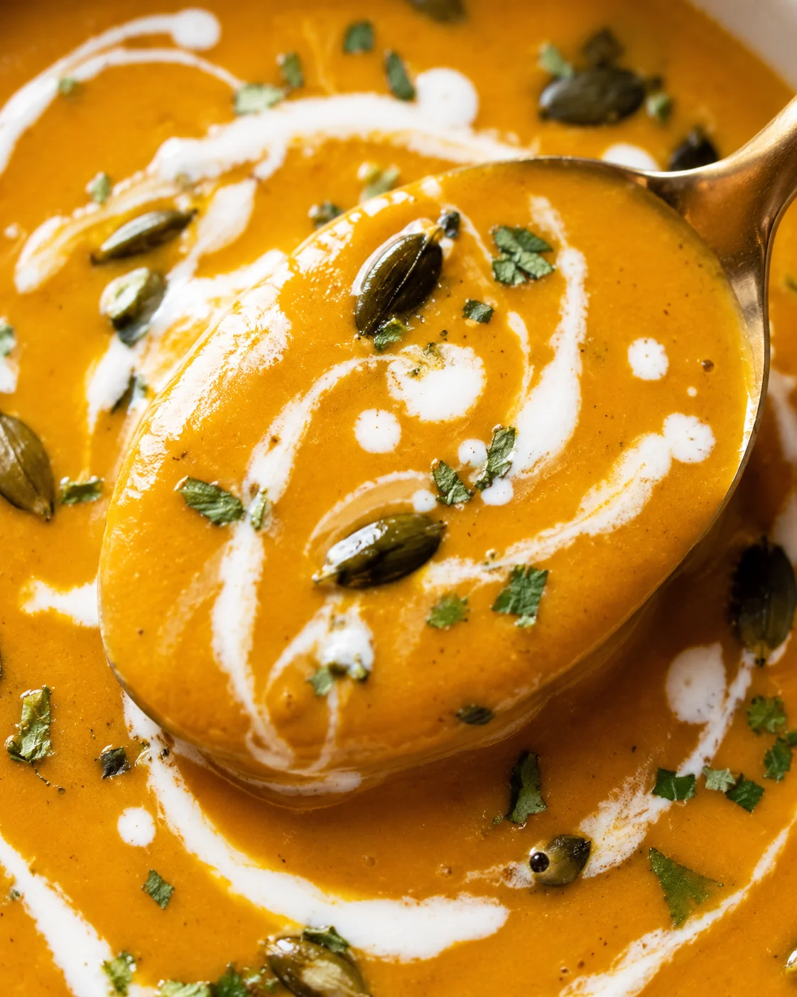 Close-up of creamy pumpkin curry soup topped with pumpkin seeds and cilantro.