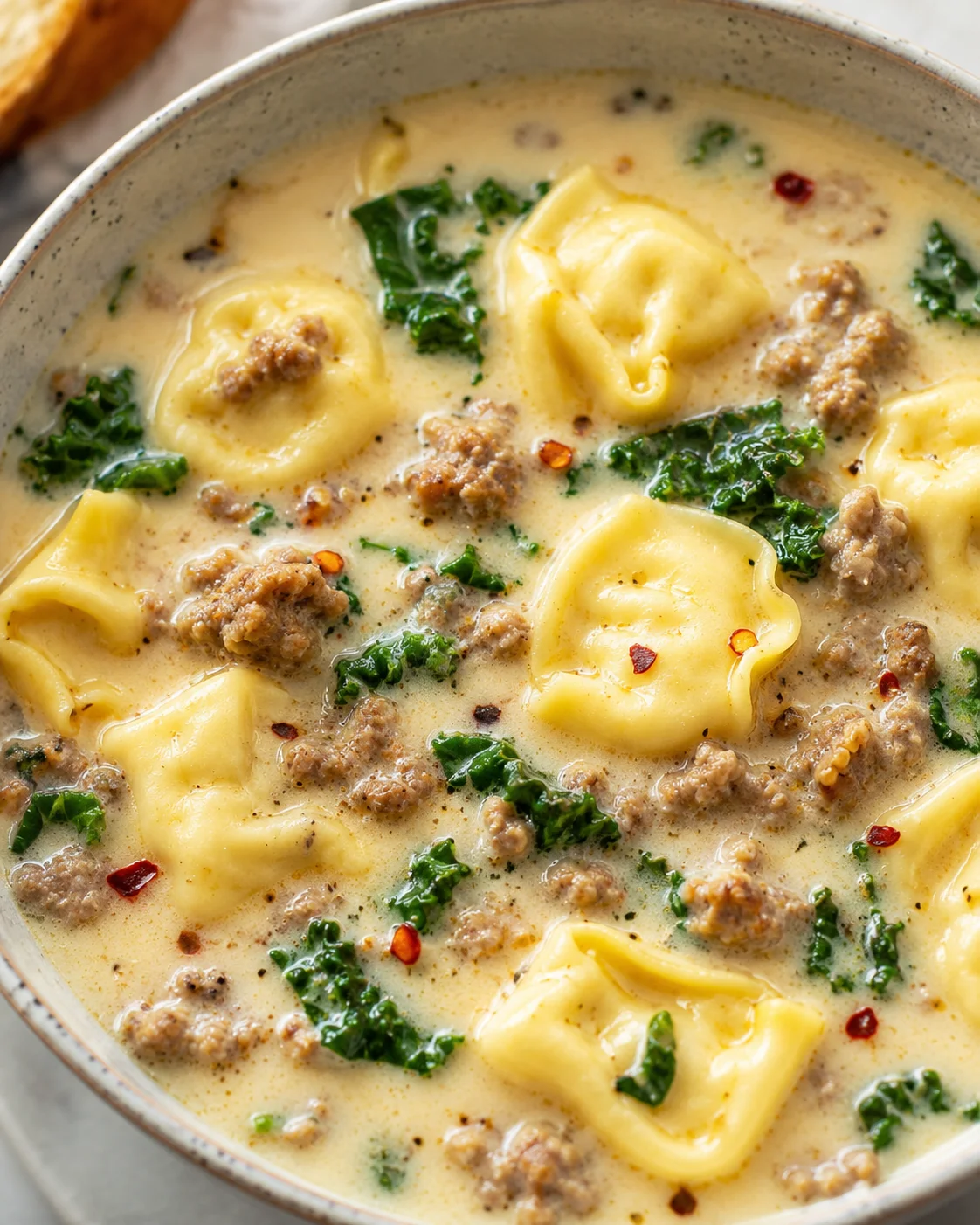 Bowl of creamy sausage tortellini soup with kale and crumbled sausage